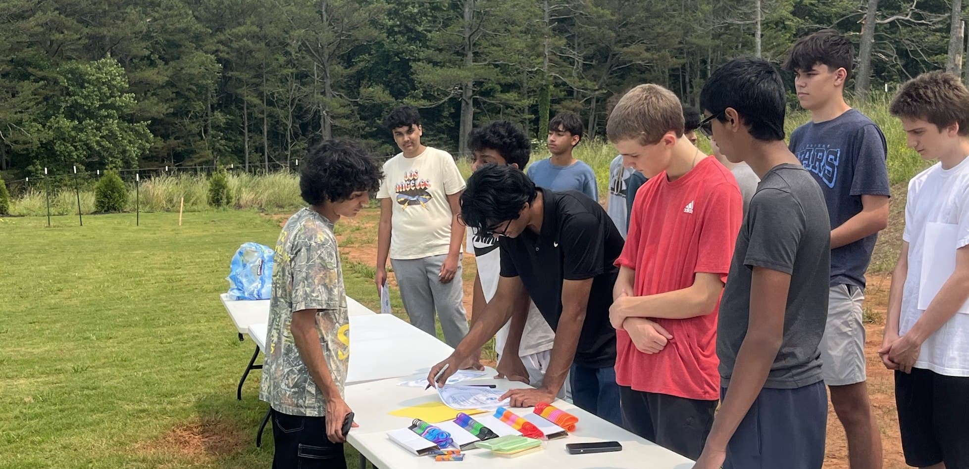 Hands of Hope students gathered around the supply tables at an outdoor packing event